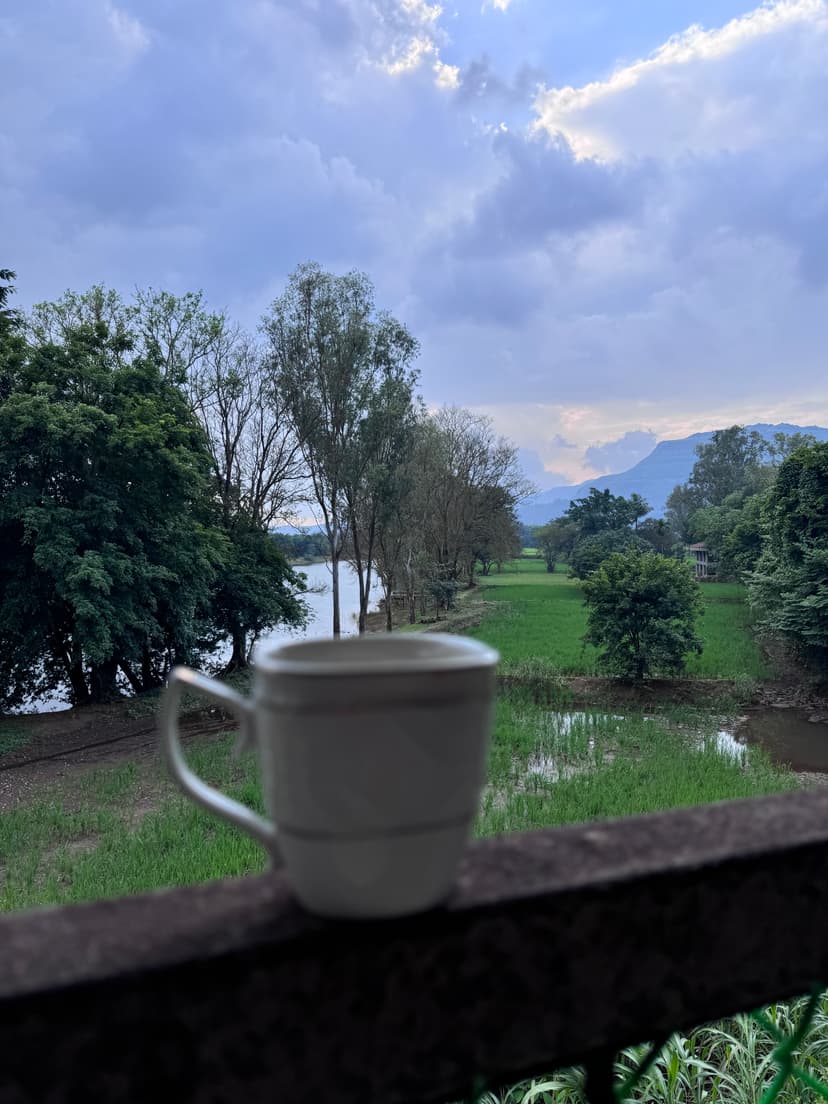 Coffee cup on a balcony railing with scenic view of river, trees, and distant mountains