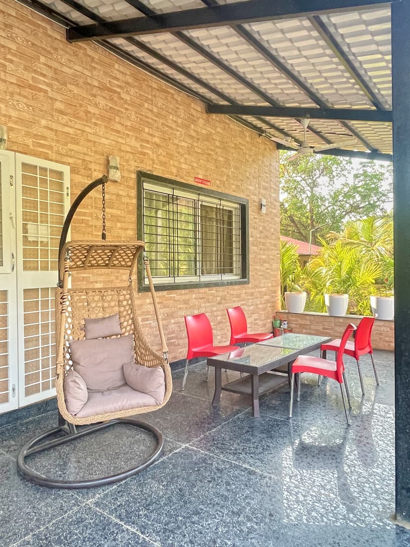 Front patio with swing chair, red chairs, and glass-top table outside Kokan Kinara Villa