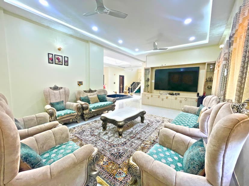 Spacious living room at Kokan Kinara with ornate sofas, carpet, and a large TV unit